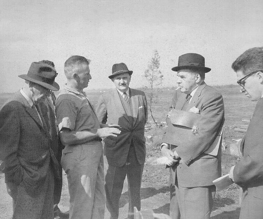 Thomas E Lee, archéologue, et un groupe d'hommes discutant lors des fouilles archéologiques pour retracer les vestiges du combat du Long-Sault à Hawksberry en 1961