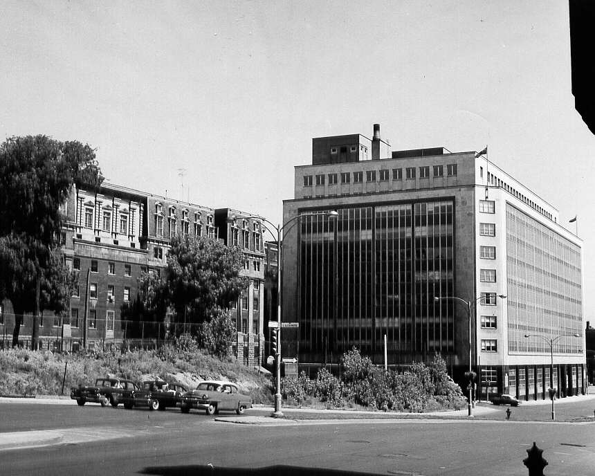 À Montréal en 1961, des automobiles à un feu rouge sur la rue Dorchester et deux édifices en arrière-plan 